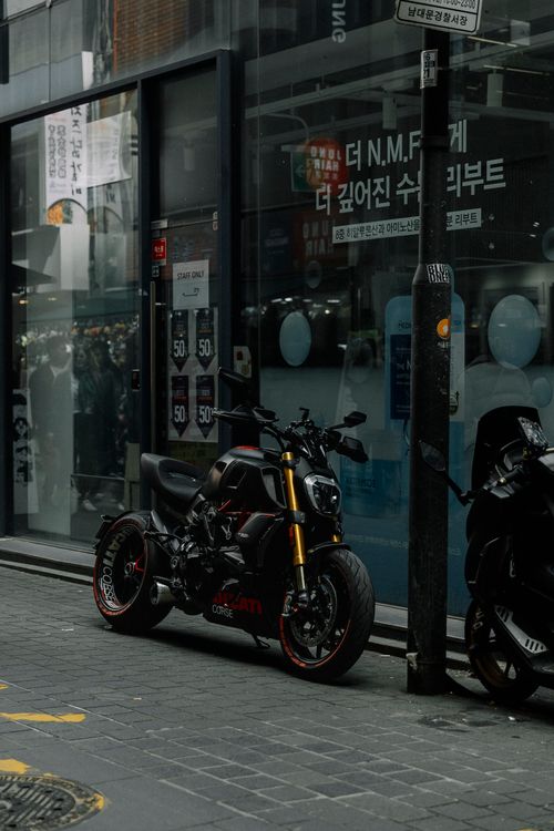 Free A stylish black Ducati motorcycle parked on a city street corner, showcasing modern urban lifestyle. Stock Photo