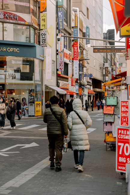 Fotomural Pareja caminando en un vibrante distrito comercial en Seúl durante el invierno, rodeados de carteles de oferta y edificios.