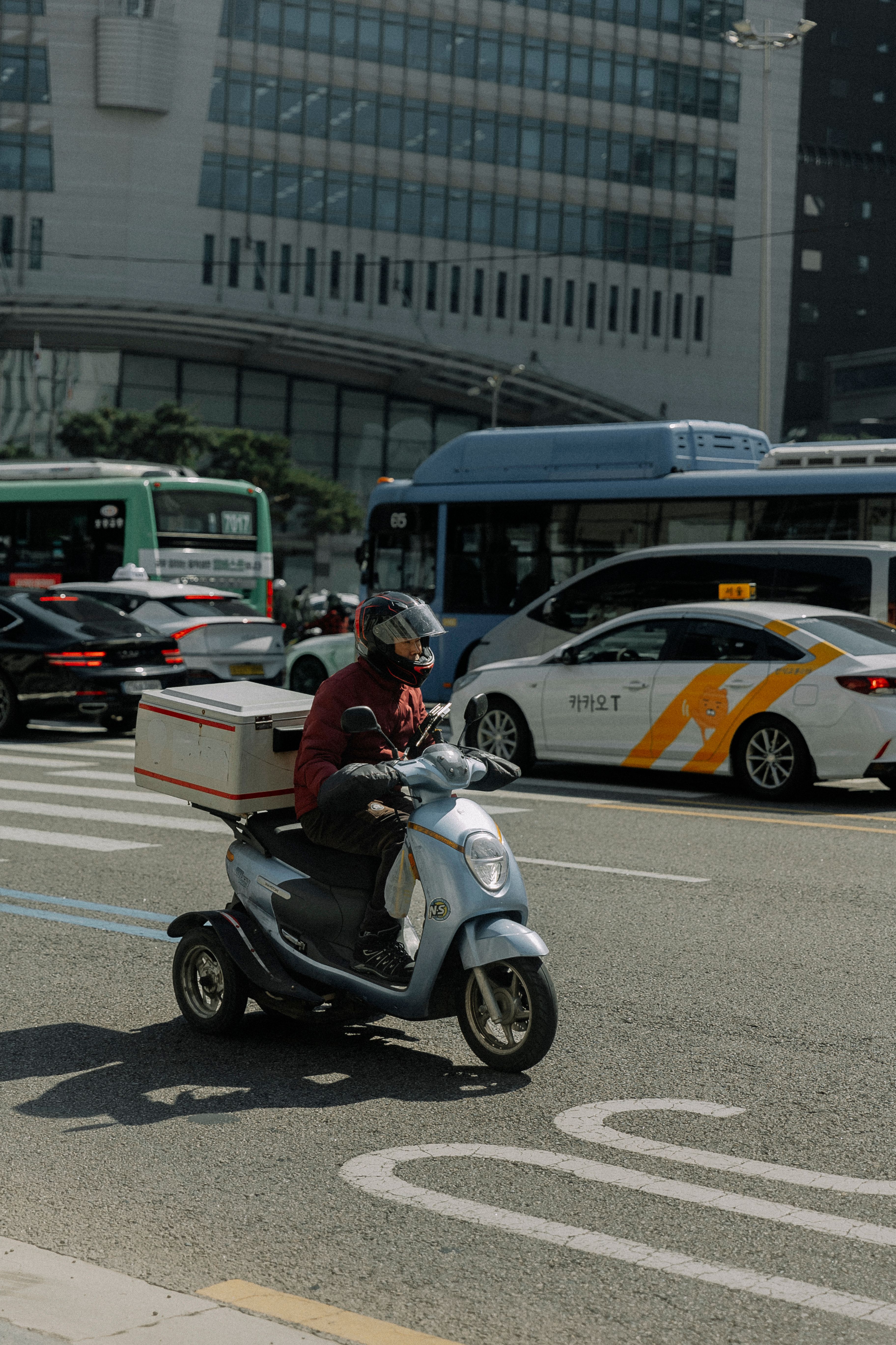 Courier on a scooter navigating through busy urban traffic during the day.