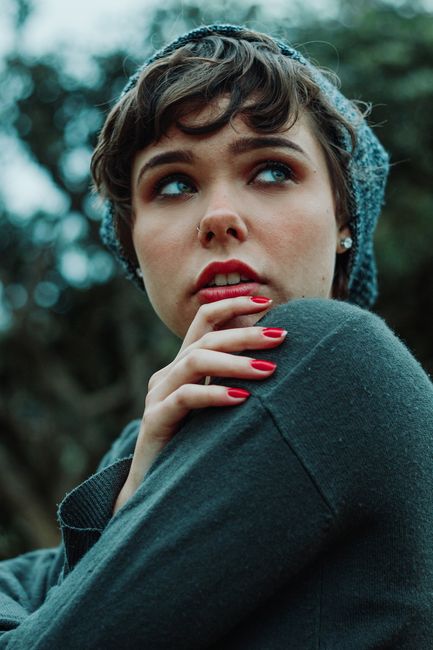Stylish woman posing with red nails and grey beanie in a natural setting.