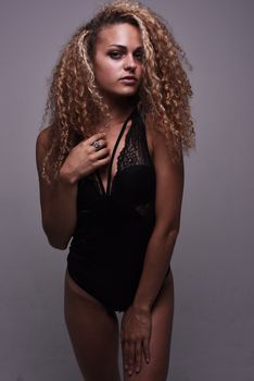 Model posing confidently in a lace bodysuit in a studio setting, showcasing curly hair and fashion style.