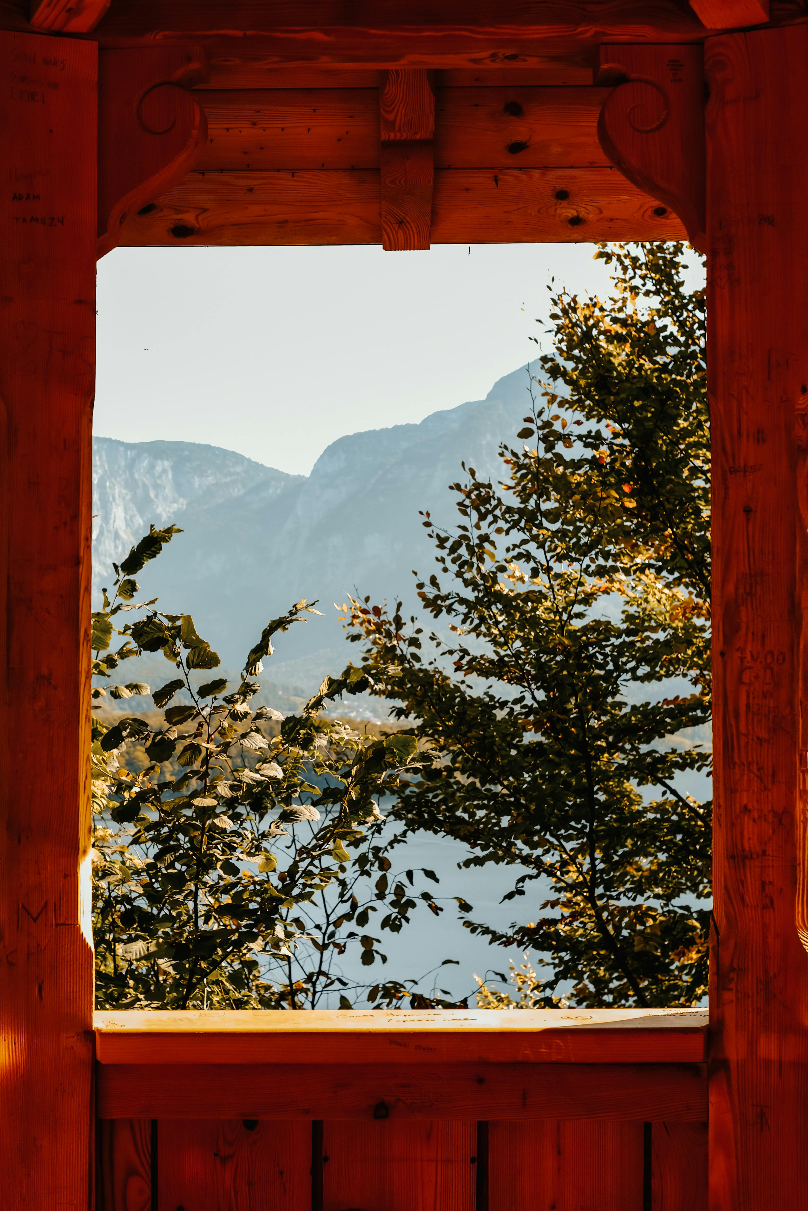 Serene view through a wooden window frame showcasing Hallstatt's picturesque mountain landscape.