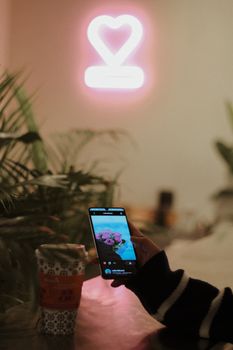 A cozy setup with a neon heart, mobile phone, coffee cup, and plants.