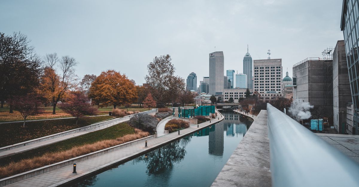 Scenic view of Indianapolis canal with city skyline and autumn colors reflecting on the water.