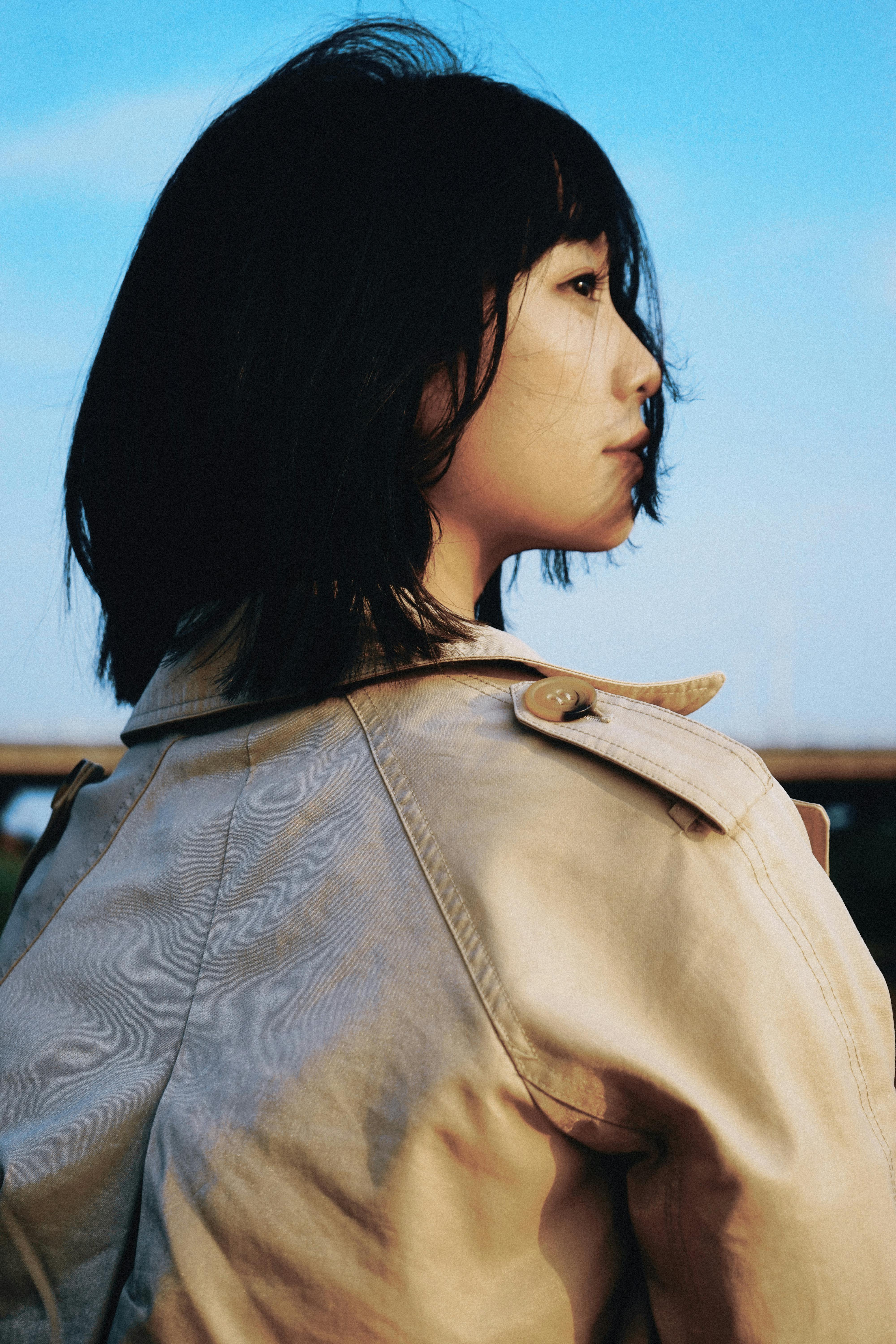 Profile shot of a woman in a beige coat, gazing contemplatively outdoors.