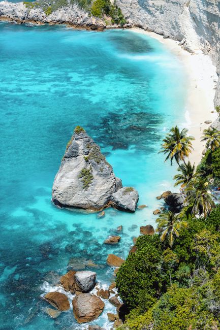 Stunning aerial shot of a rocky tropical beach with turquoise waters, lush greenery, and a unique rock formation.