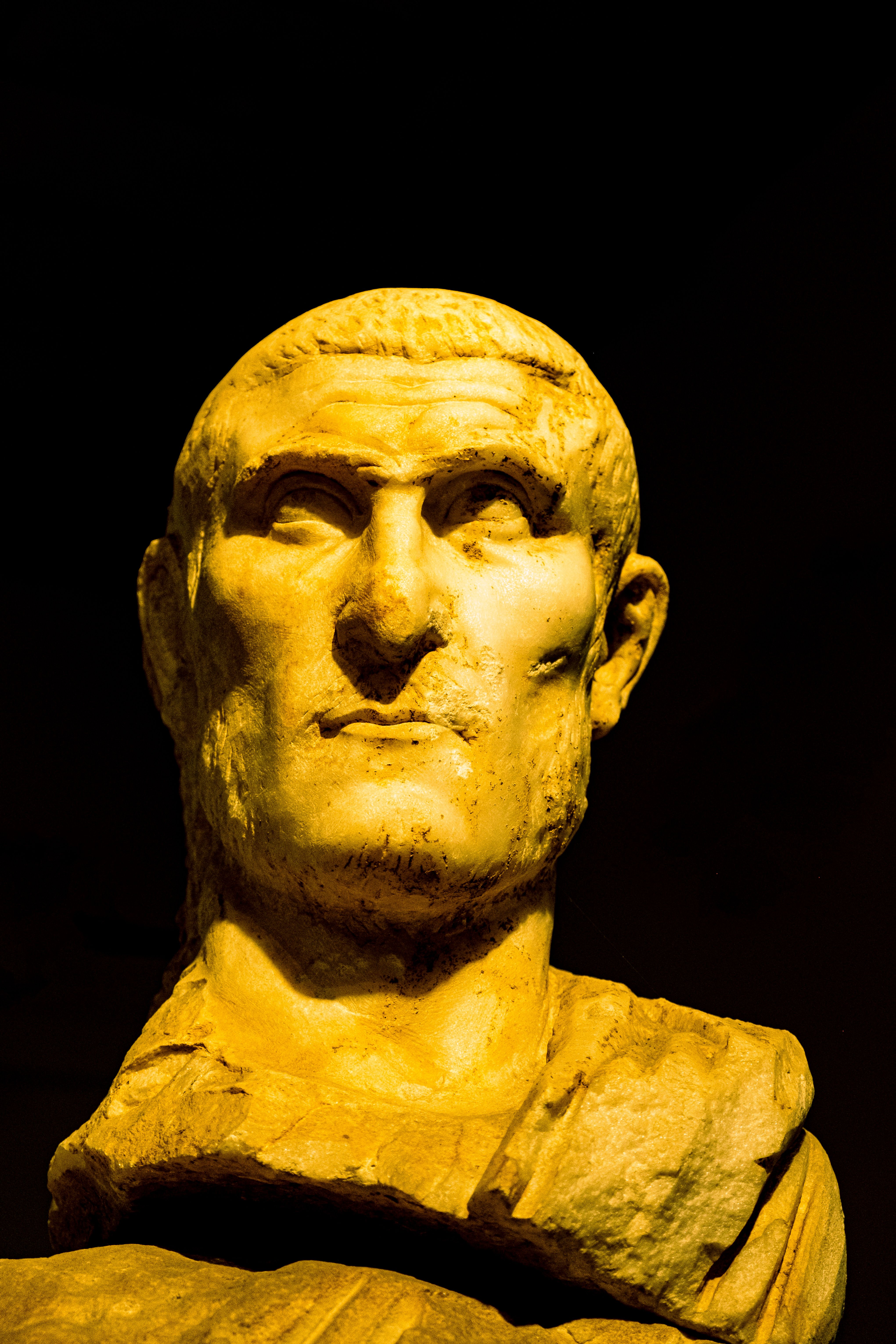 A classic Roman bust in golden tones illuminated dramatically against a dark backdrop.