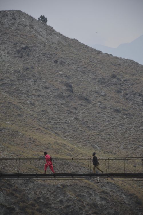 Free Two people crossing a suspension bridge in a rugged mountain landscape. Stock Photo