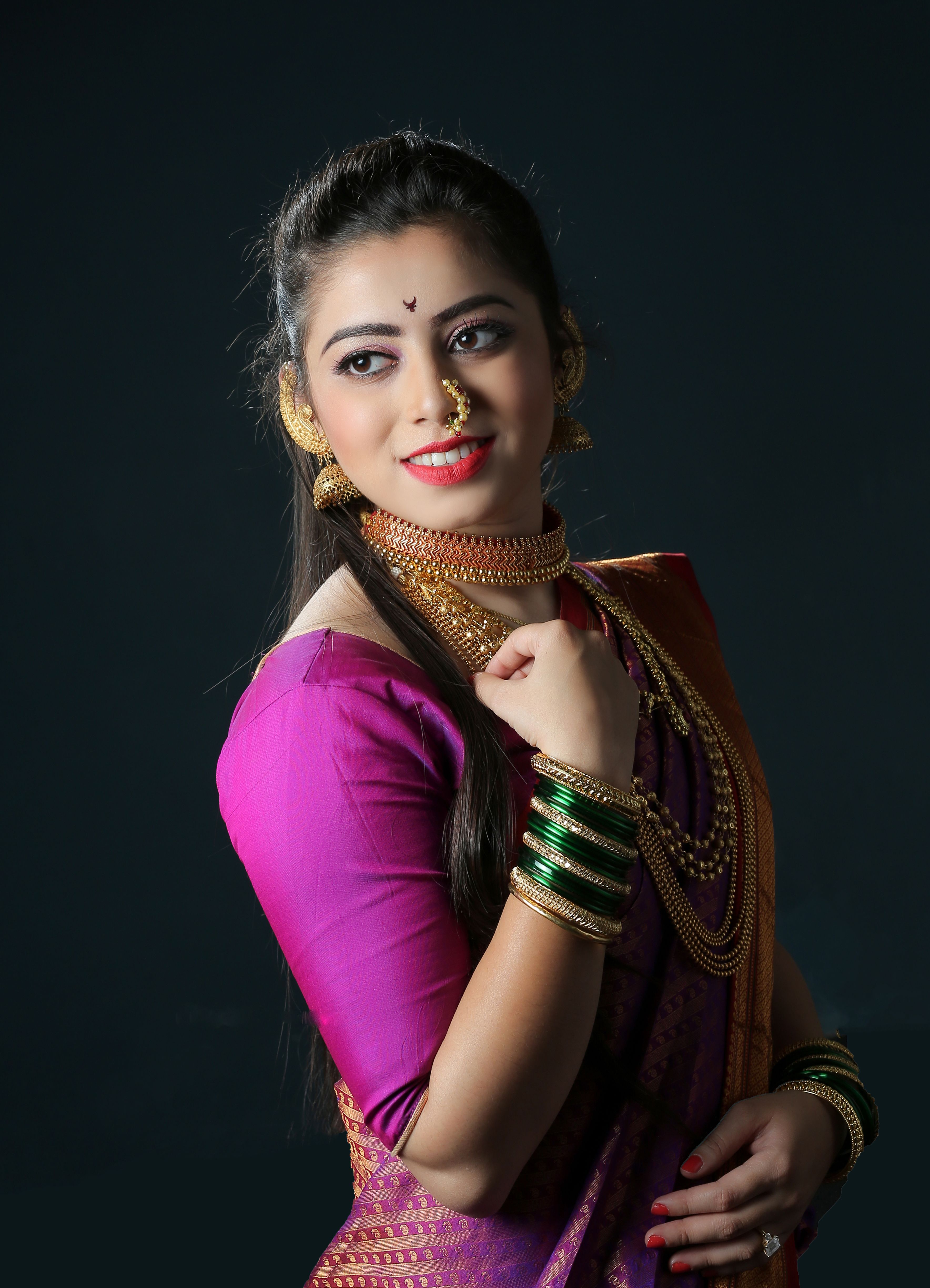 A young woman wearing Indian traditional clothing and jewelry, smiling confidently.