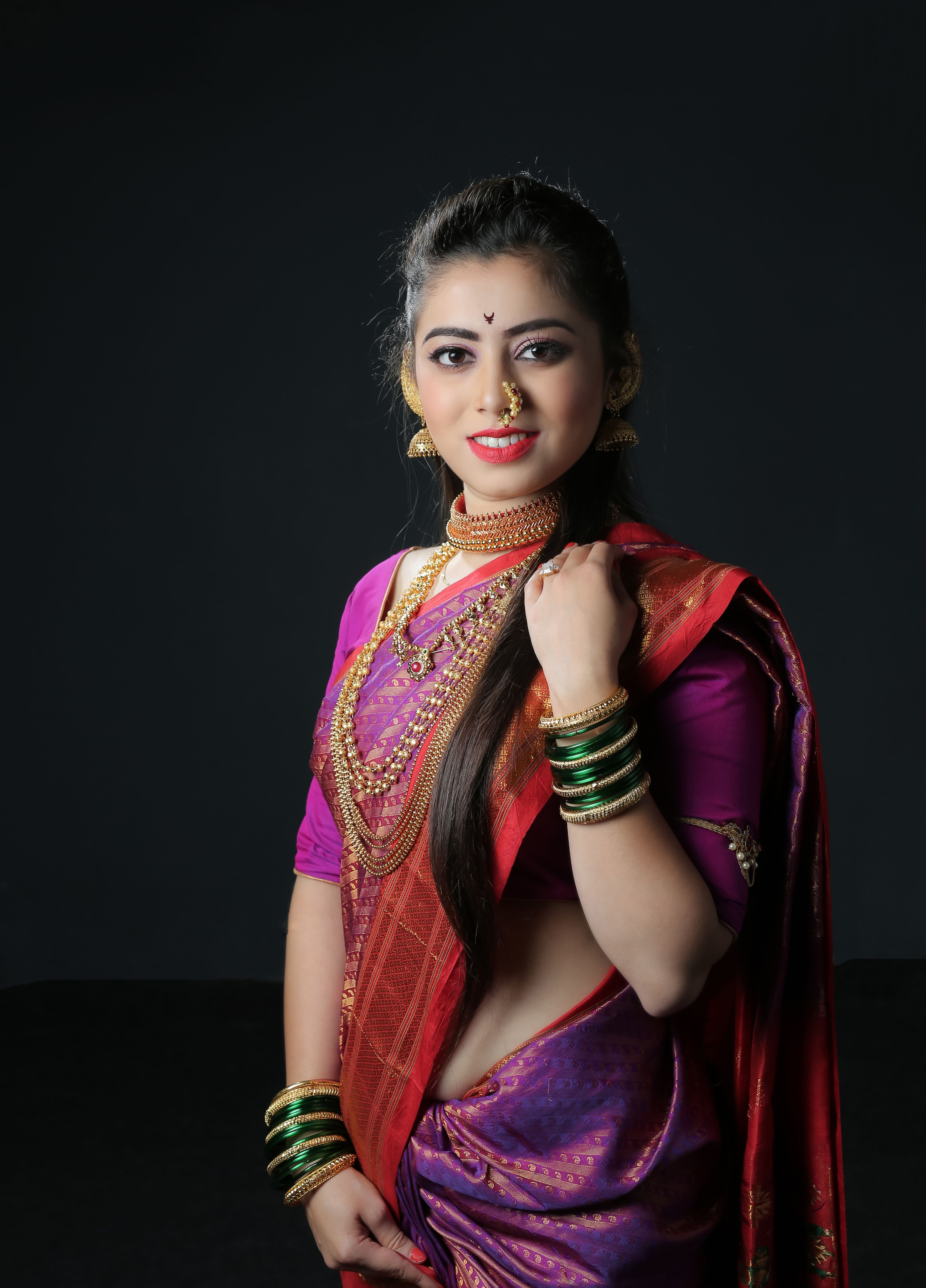 Portrait of a young woman in vibrant Indian attire with jewelry, smiling confidently.