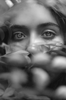 这幅迷人的黑白肖像描绘了一位女子透过树叶窥视的眼睛