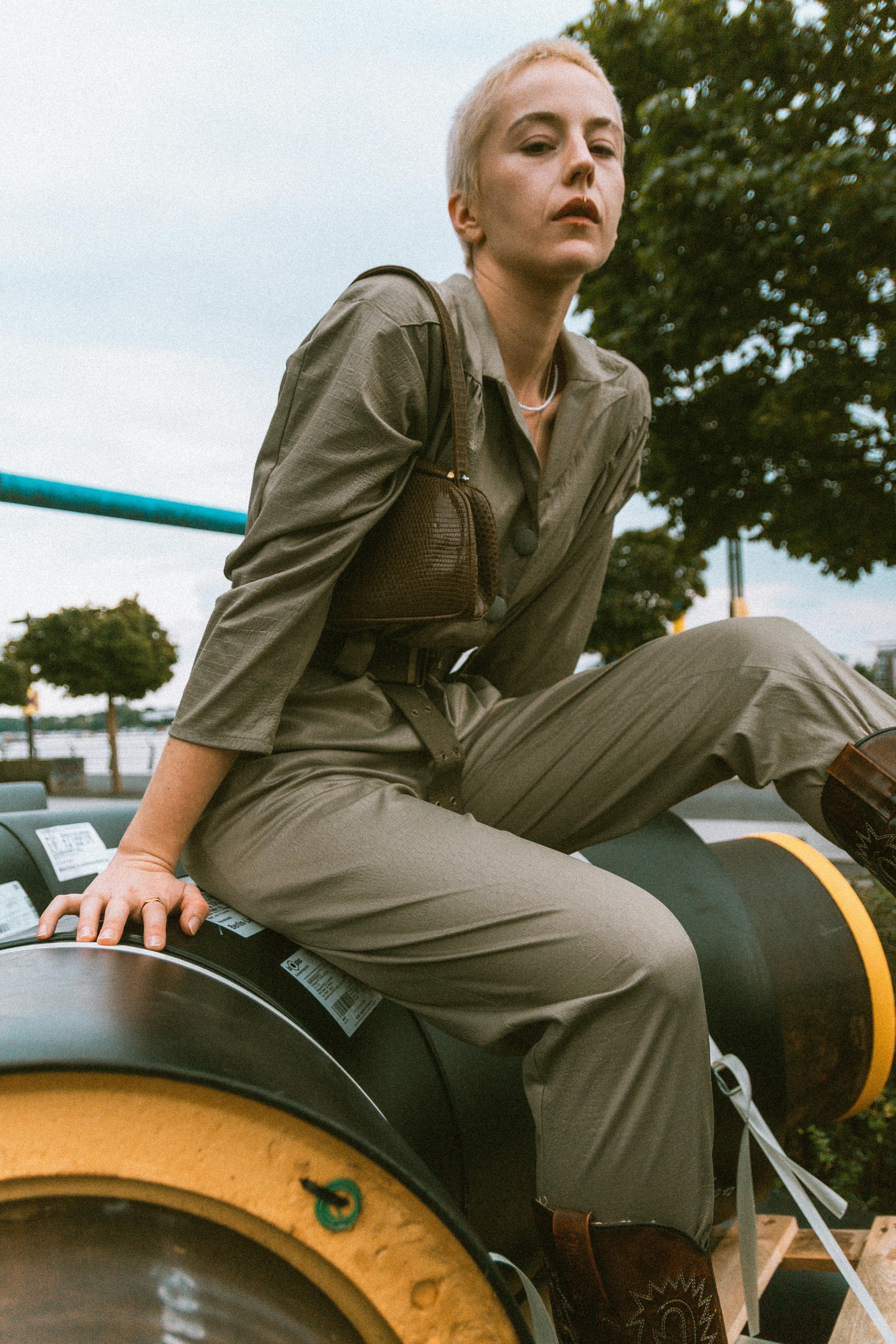 Free Stylish woman in a jumpsuit posing on industrial pipes in Berlin for a modern outdoor fashion shoot. Stock Photo