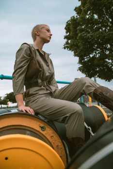 Stylish woman in green jumpsuit posing outdoors in an urban setting with an industrial backdrop.