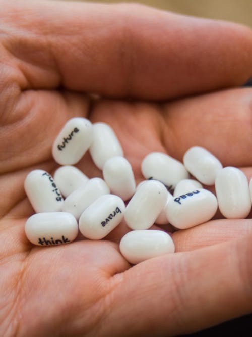 A person holding a handful of white pills with the words think