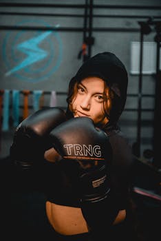 Focused female boxer wearing hood and gloves in an indoor gym environment.