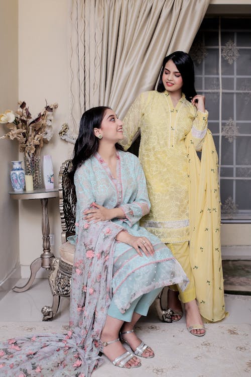 Two women in yellow and green dresses sitting on a couch