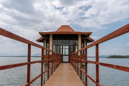 Free Wooden pier leading to a scenic lakeside pavilion under a cloudy sky. Stock Photo