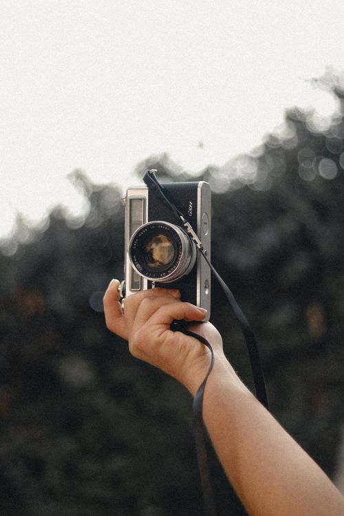 Free A hand holding a vintage camera against an outdoor blurred background. Perfect for photography themes. Stock Photo