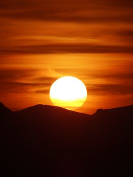 Vibrant sunset with a glowing orange sky over silhouetted mountains.