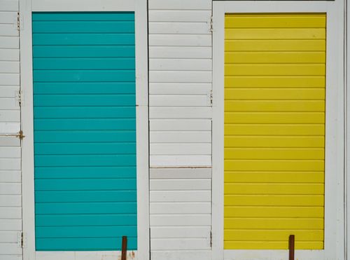 Free Close-up of bright turquoise and yellow wooden doors on a white wall. Stock Photo
