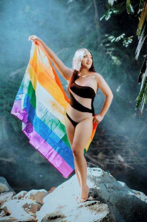 A woman in a black swimsuit holding a rainbow flag