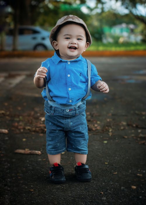 A young boy in blue shirt and suspenders standing on the street