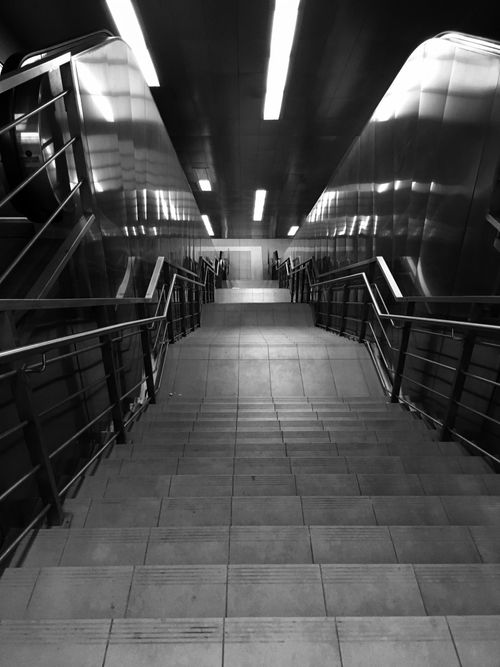 Free Black and white image of an underground staircase in an urban environment showing perspective and symmetry. Stock Photo