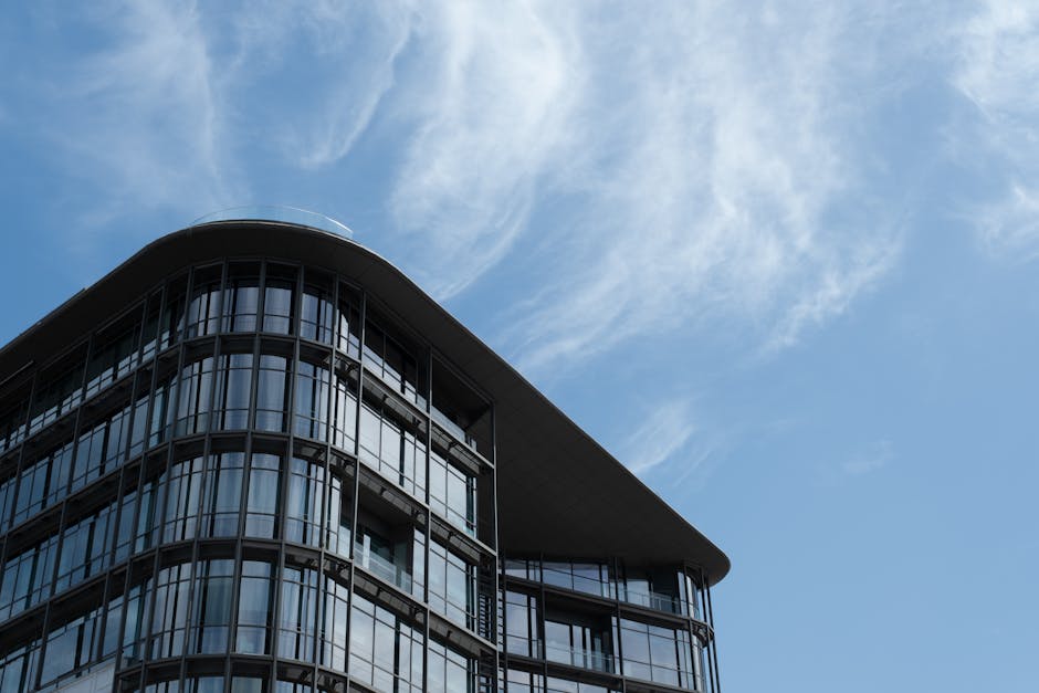 Architectural shot of a sleek modern office building with large glass windows under a clear blue sky.