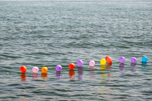 Free Vibrant balloons float on the ocean water, creating a cheerful and scenic view. Stock Photo