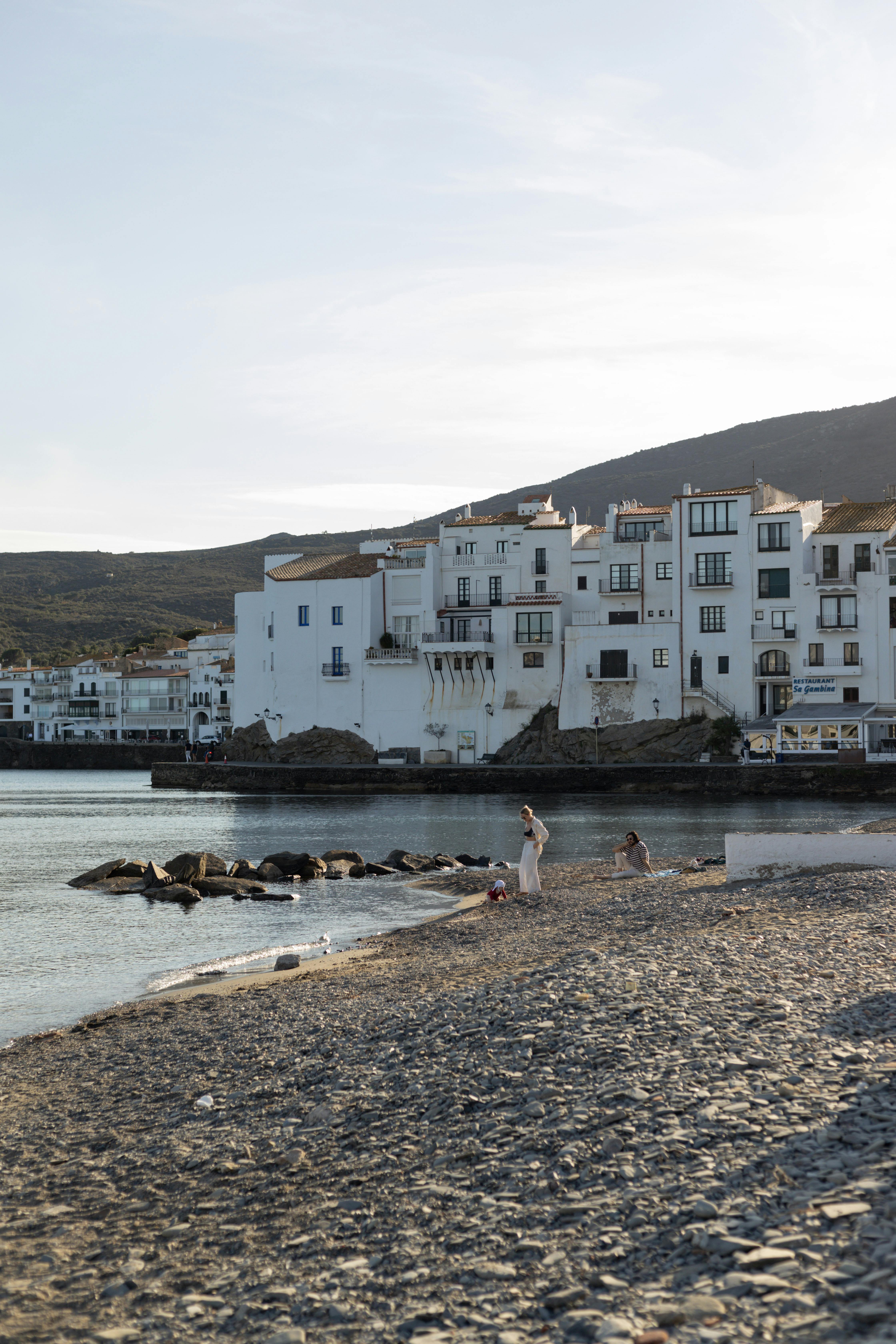 Relaxing scene at rocky Cadaqués beach with iconic white houses under summer sunlight.