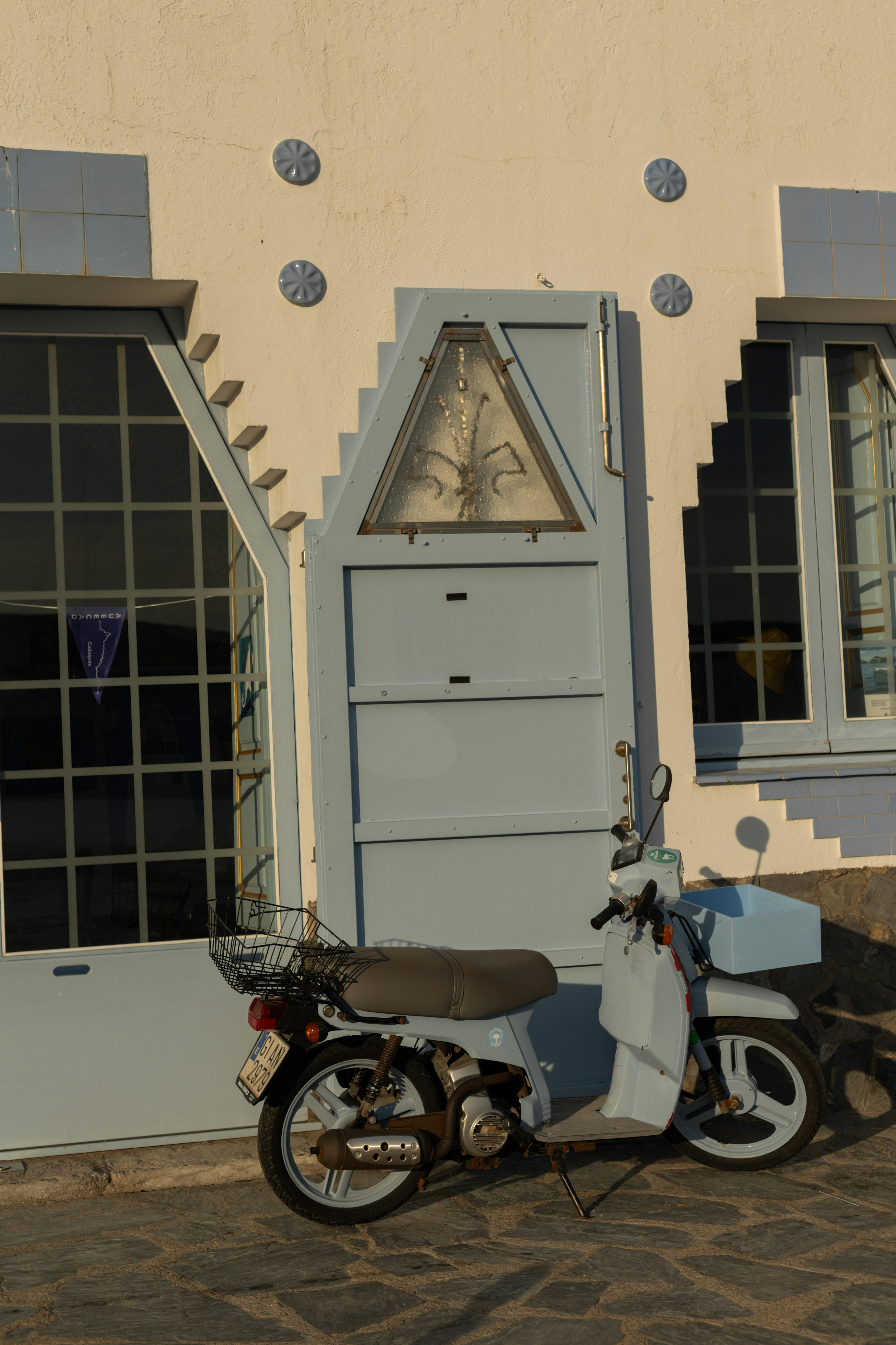 A charming scene capturing a vintage scooter parked by a unique geometric door in Cadaqués, Spain.