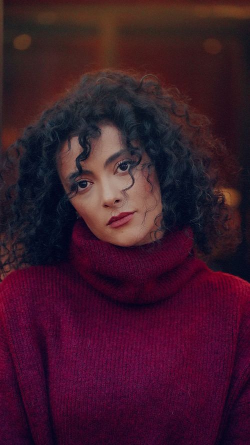 Free Portrait of a woman with curly hair wearing a red turtleneck sweater, exuding warmth and style. Stock Photo