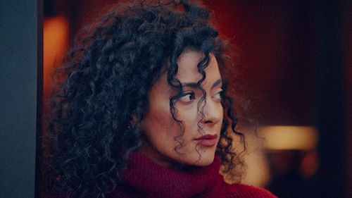 Free A woman with curly hair looks to the side, wearing a red sweater indoors. Stock Photo