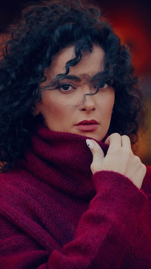 Free Close-up portrait of a woman in a red turtleneck sweater with curly hair, looking confidently into the camera. Stock Photo