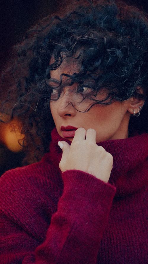 Free Portrait of a thoughtful woman wearing a red sweater with curly hair covering her face. Stock Photo