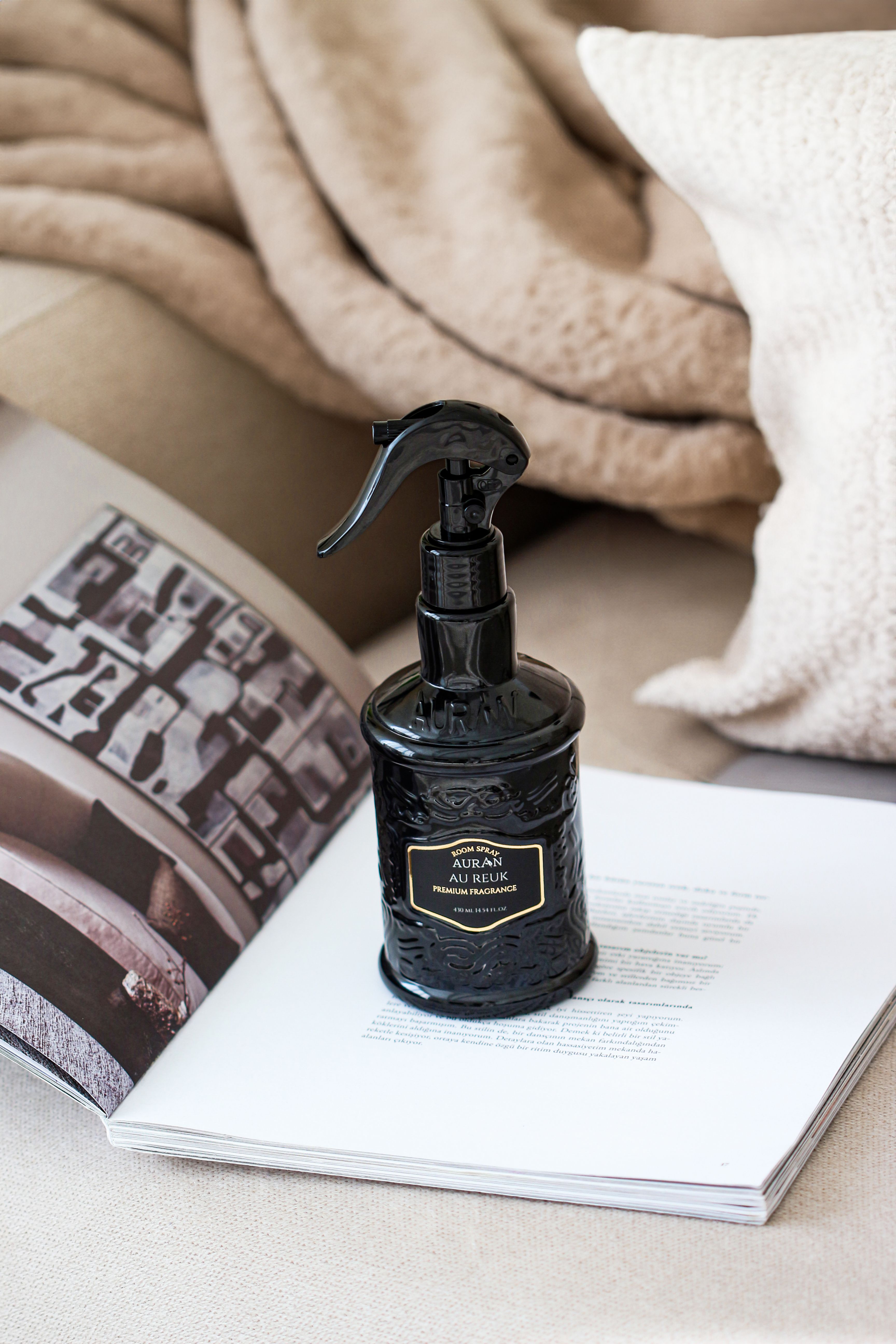 Black spray bottle elegantly placed on an open magazine with a cozy blanket backdrop.