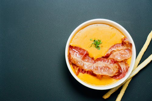 A bowl of soup with bacon and bread sticks