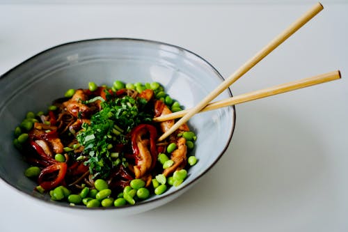 A bowl of food with chopsticks and peas