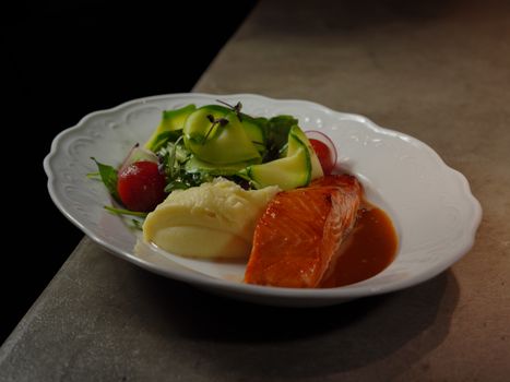 Elegant plate of salmon, mashed potatoes, and fresh vegetables on a gourmet dish.