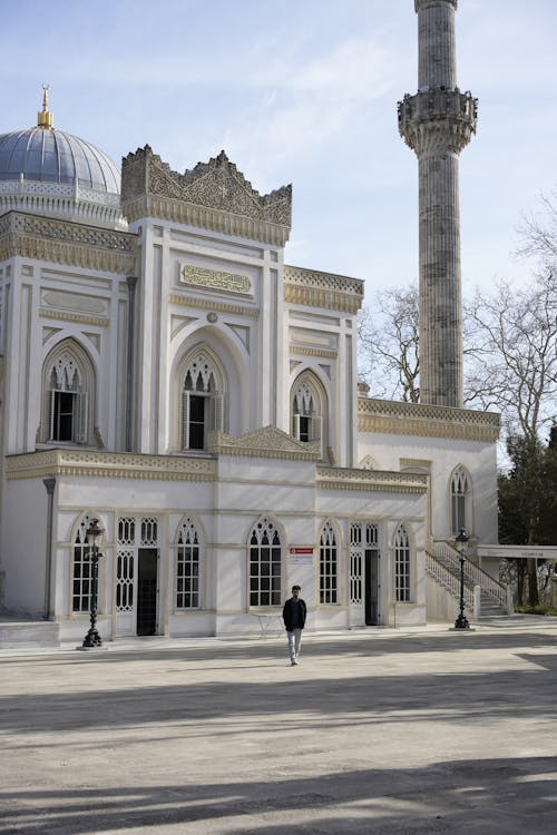 A man walks past a white mosque with a clock tower