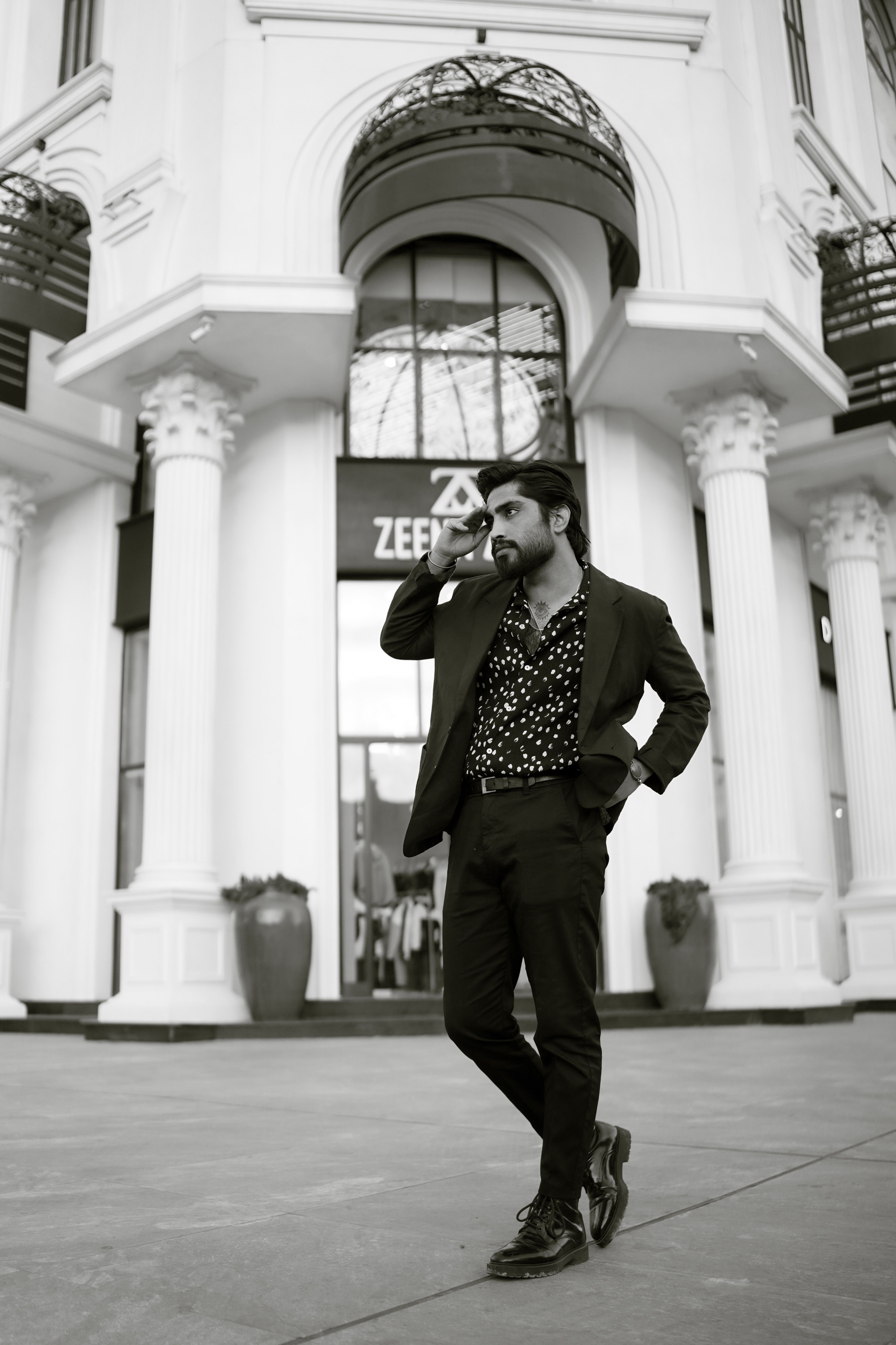 Man in a fashionable suit posing in monochrome city setting.