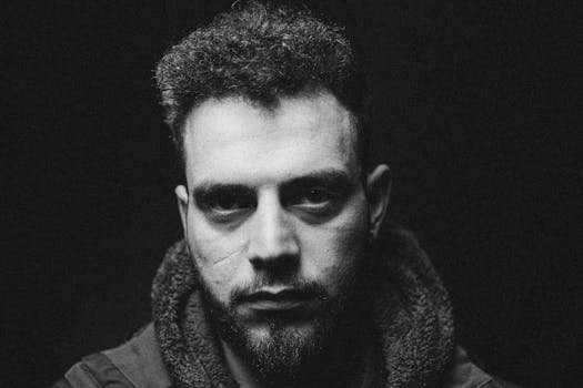 Dramatic black and white portrait of a man with curly hair and a beard.