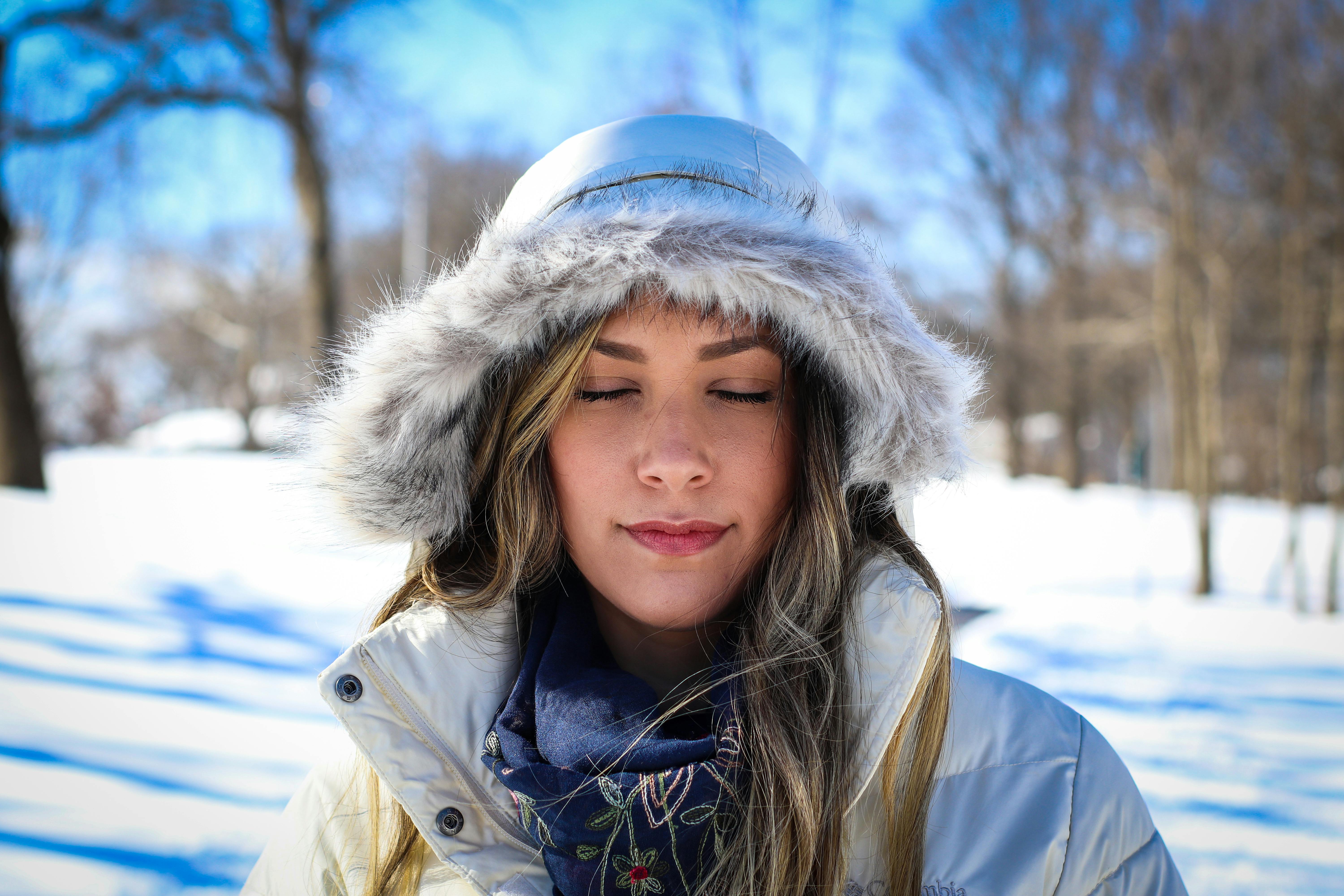 冬日雪景中，一位身着毛皮连帽外套的女子闭目肖像