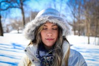 冬日雪景中，一位身着毛皮连帽外套的女子闭目肖像