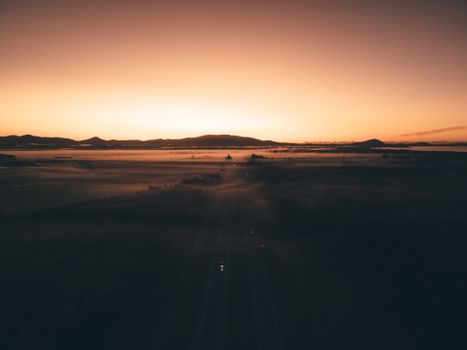 A breathtaking aerial view of a serene sunset over hills and misty plains creating a mystical and calm atmosphere.