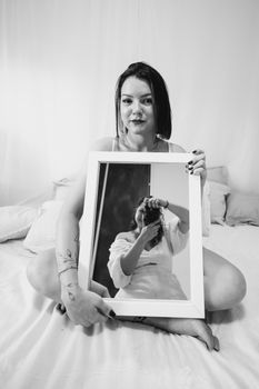 Woman holds a mirror reflecting herself in a black and white portrait.