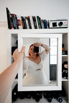 Woman in white dress capturing her reflection in a mirror holding a camera.