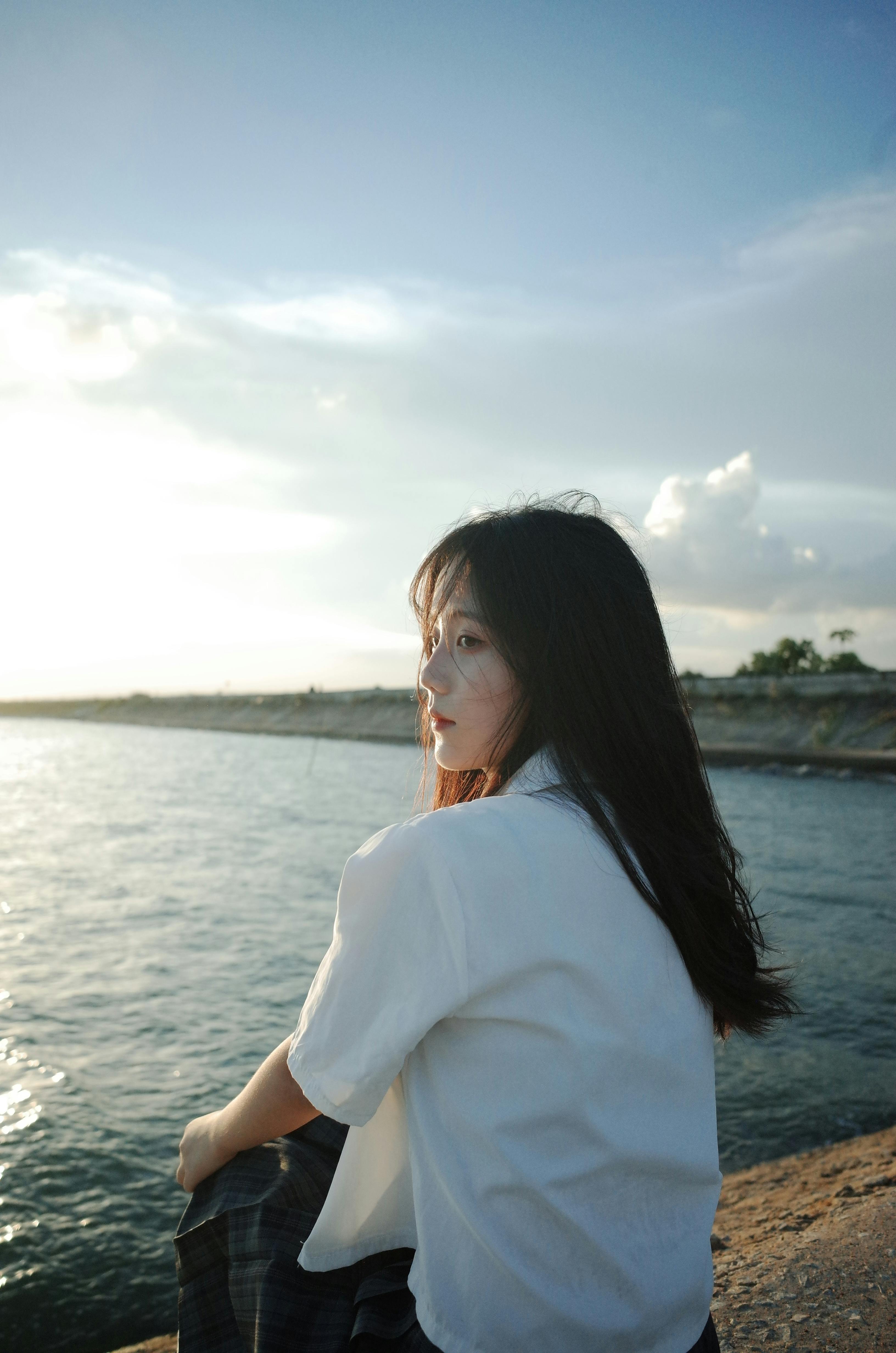 Serene image of a young woman sitting by the sea, enjoying a peaceful sunset moment.
