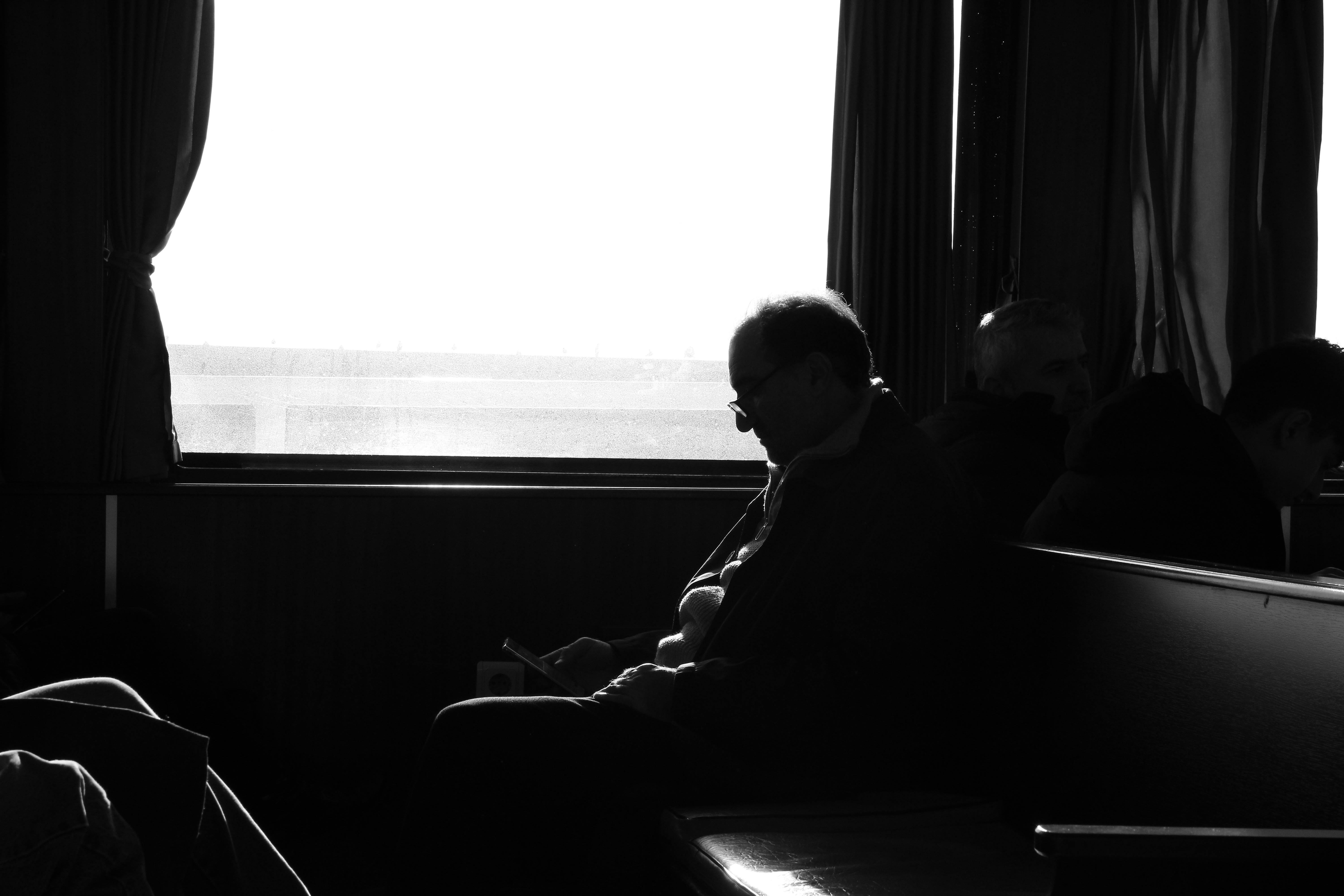 A black and white photo capturing passengers on a ferry, with silhouettes against a bright window.
