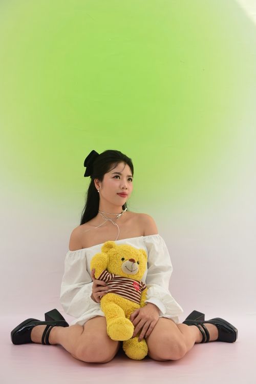 Free Asian woman posing with teddy bear against green backdrop in studio. Stock Photo